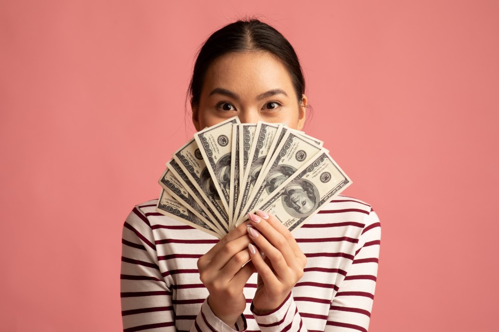 Femme d’origine asiatique heureuse qui tient de l’argent américain dans ses mains