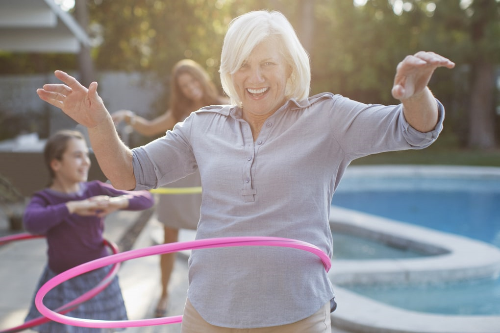 Retired woman playing spinning a hula hoop with her family.